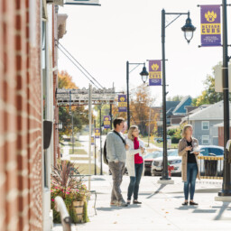 Four adults chat on a sunny downtown sidewalk in Nevada, Iowa, with purple “Nevada Cubs” banners and fall trees in the background.