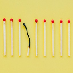 Row of matches on a yellow background with one burned match in the center.