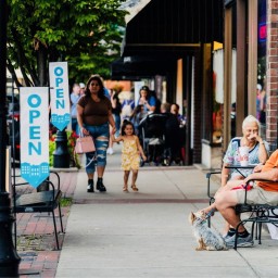 People walk, talk, and relax outside open businesses along a lively Main Street sidewalk in Bardstown, Kentucky.
