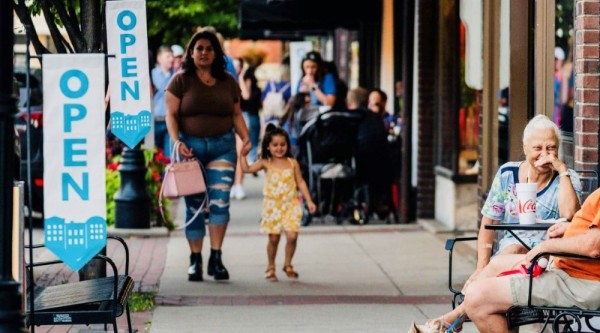 People walk, talk, and relax outside open businesses along a lively Main Street sidewalk in Bardstown, Kentucky.