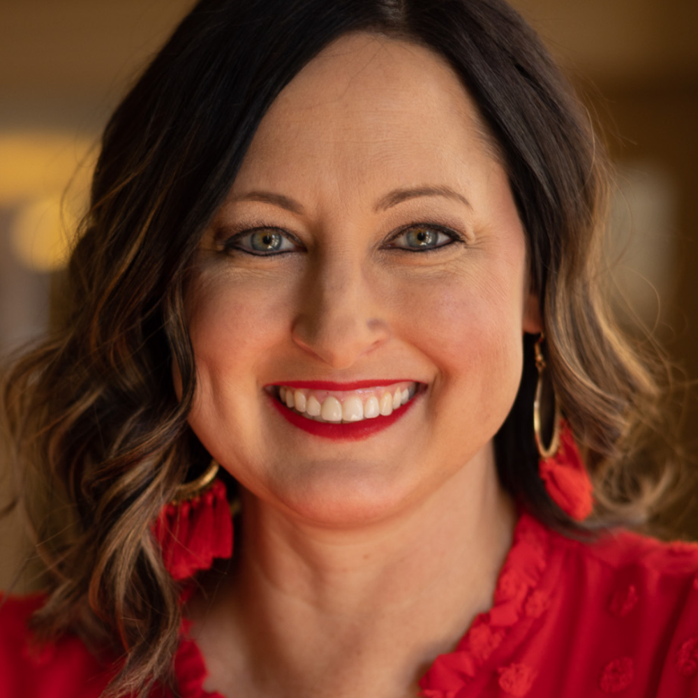 Headshot of a woman with brown hair wearing red earrings and a red dress.