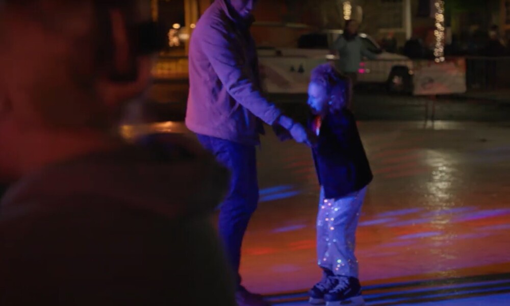 Man and young girl ice skate in a public rink.