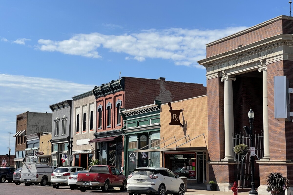 Photo of a downtown scene showing historic storefronts and a line of parked cars.
