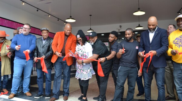 A group of people cutting a large red ribbon at the grand opening of a small business