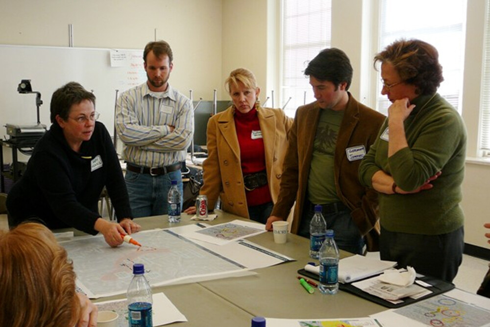 Mary Means, the "Mother of Main Street" with colleagues standing around a table mapping out a plan.