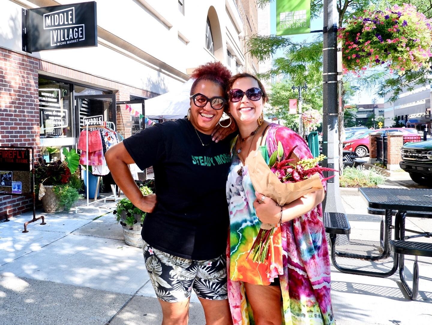 Two women smile for the camera holding flowers in downtown Lansing, Michigan.