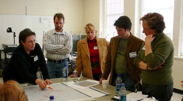 Mary Means, the "Mother of Main Street" with colleagues standing around a table mapping out a plan.