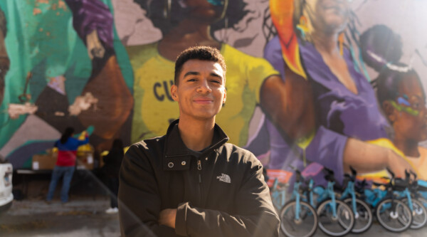 Man standing in front of a colorful mural and bikes with his arms crossed.