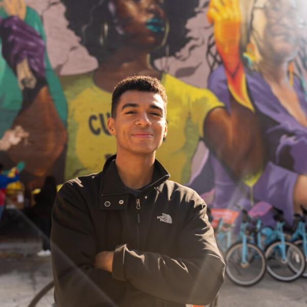 Man standing in front of a colorful mural and bikes with his arms crossed.
