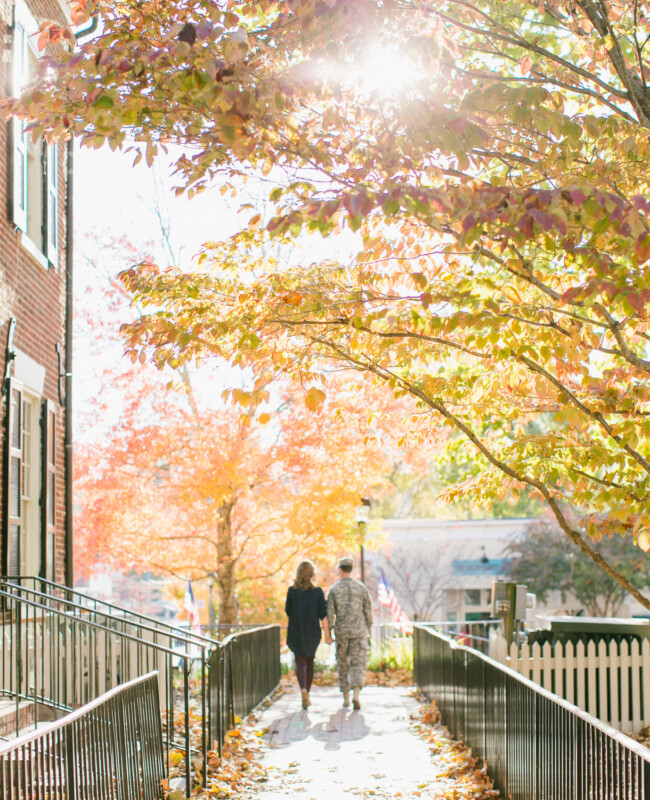 Two people walk down a tree lined street.