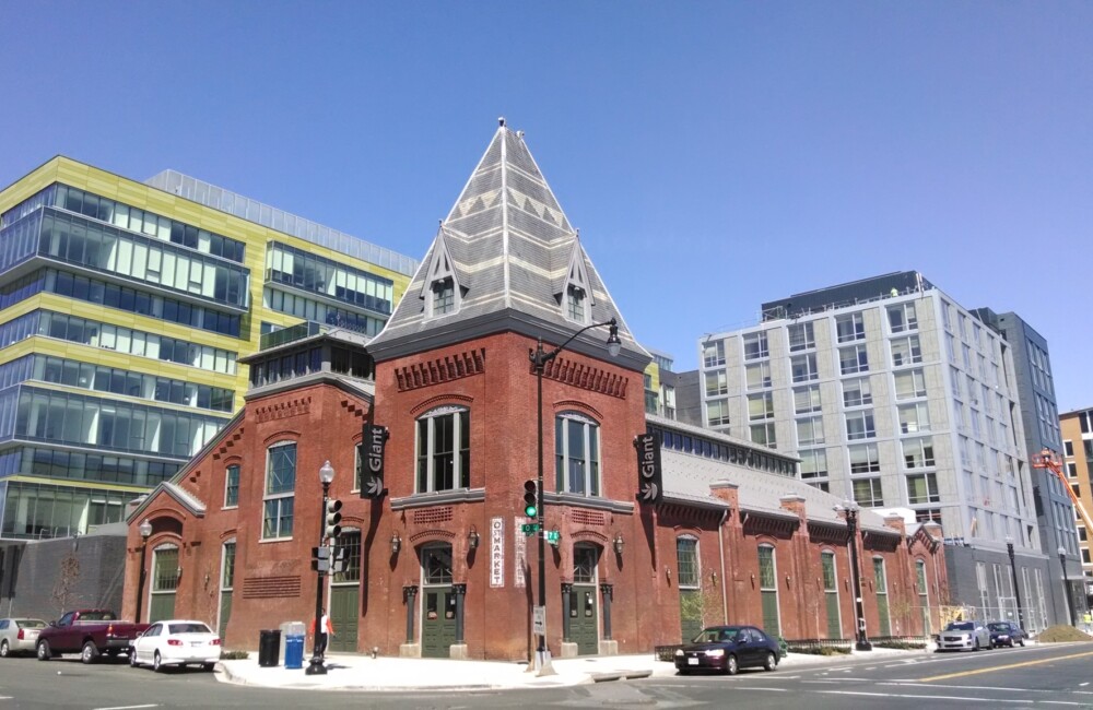 Un edificio de nueva construcción se alza detrás de un edificio histórico de ladrillo.
