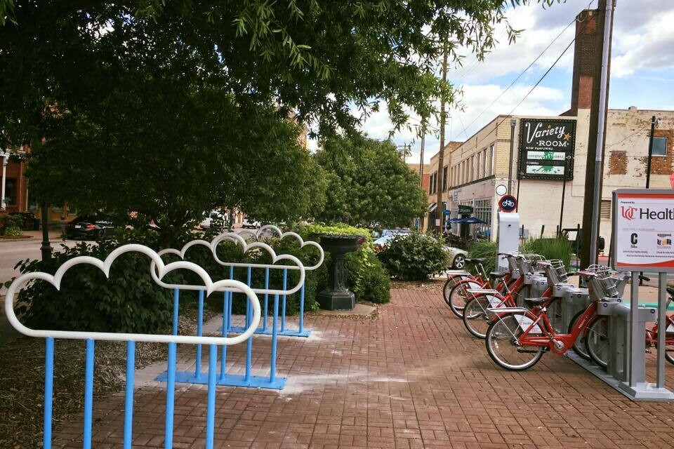 Cloud-shaped bike racks and bike-share docking station occupy a wide sidewalk.