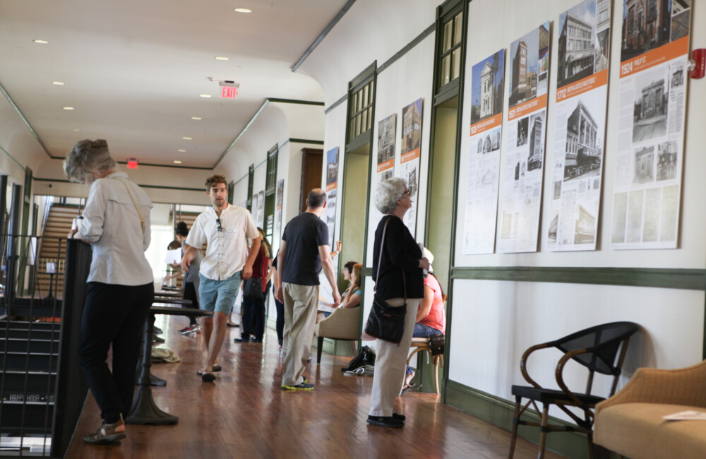 A woman examines an exhibition installation in a hallway while other people walk through the space.