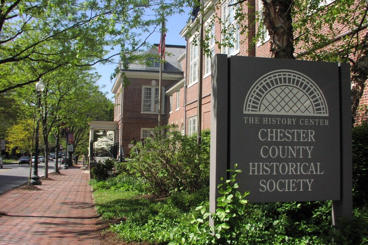 Large sign reading "Chester County Historical Society" (foreground) with a two-story brick building behind it.