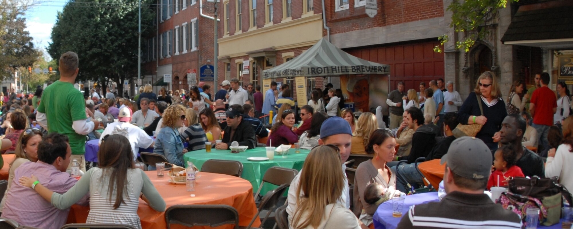 People sit at large round tables set-up in the middle of a street.