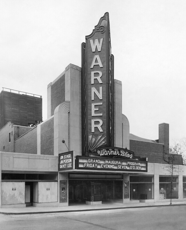 Mid-century modern movie theater with a large vertical marquee reading "Warner."