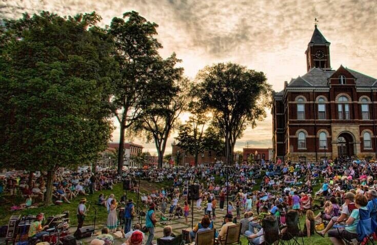 A large crowd of people gather on a grassy lawn in front of a old brick building.