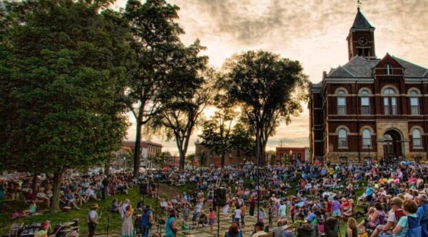 A large crowd of people gather on a grassy lawn in front of a old brick building.