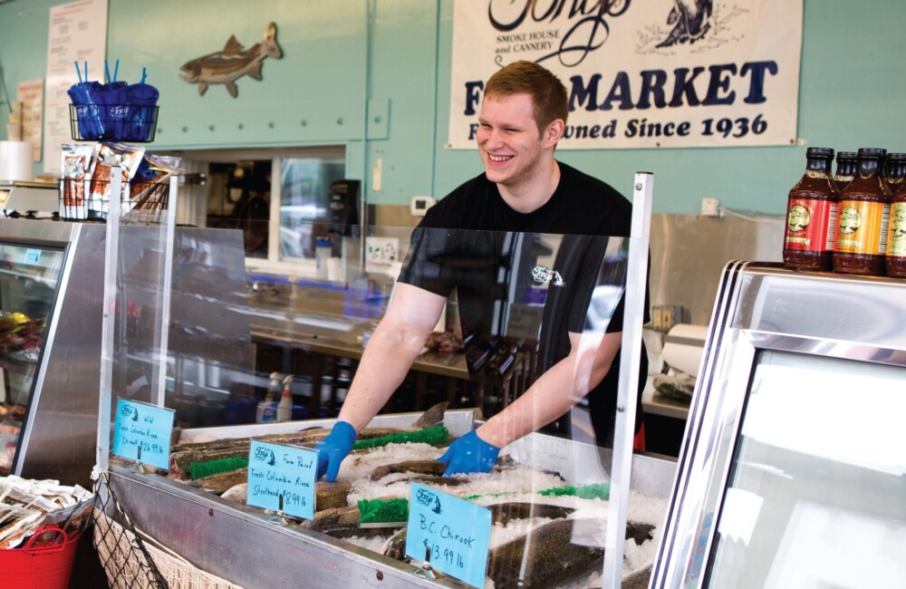 A man smiles while selecting a fish from a seafood display case.