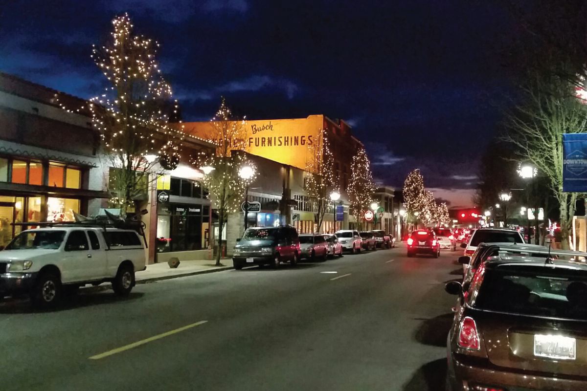 Trees lining a downtown street illuminated with string lights at night.