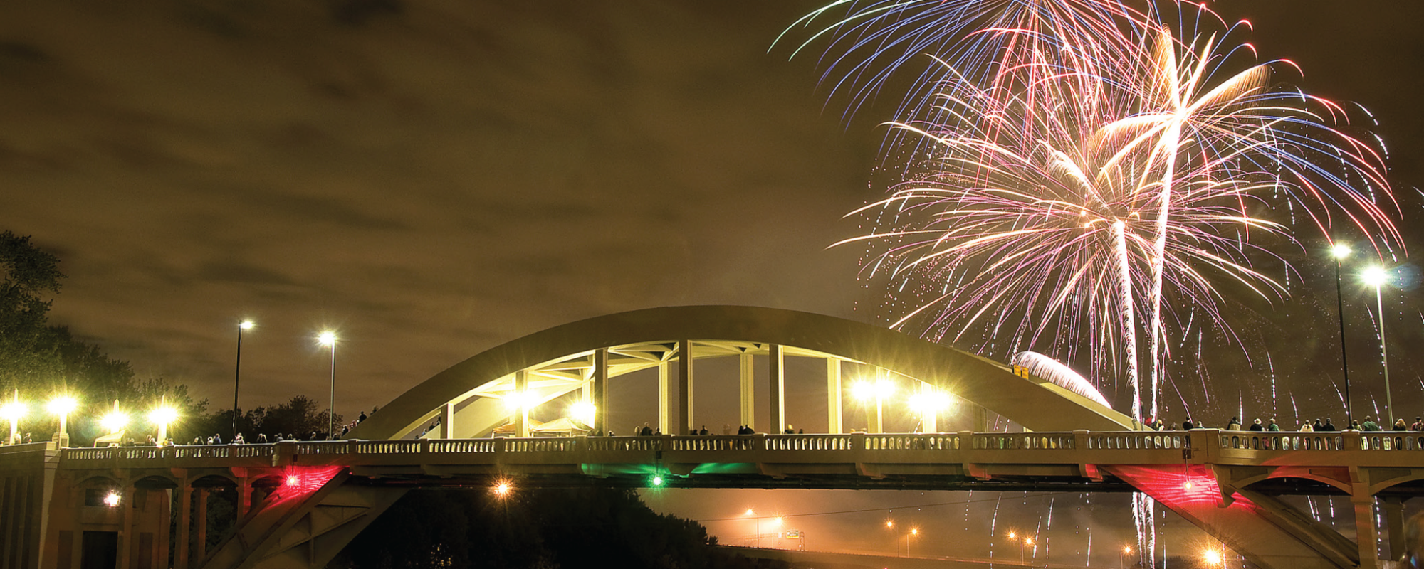 Fireworks burst above a bridge at night.
