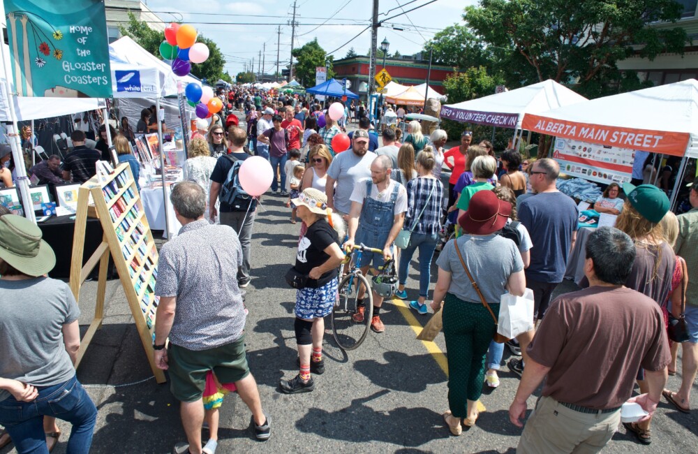 People of all ages stroll down a street flanked with pop-up vendor booths during a festival.