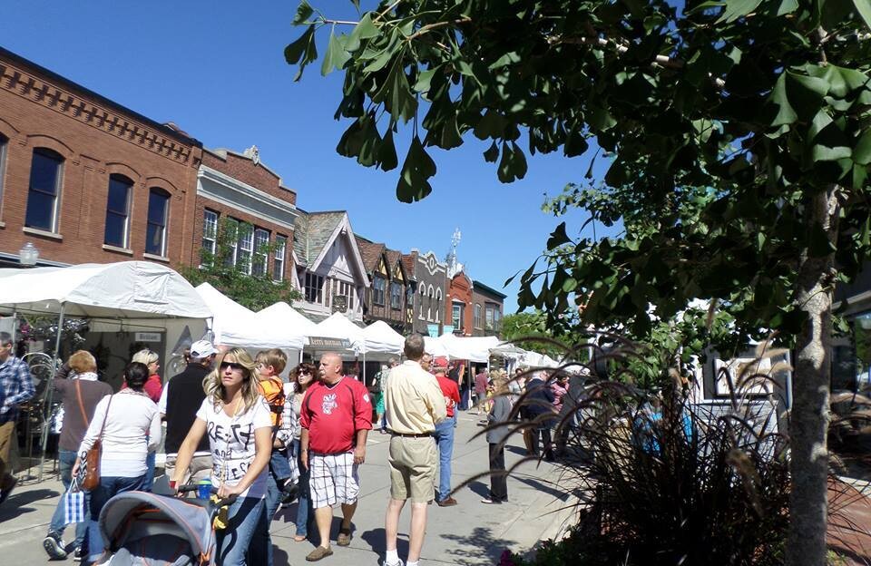 People stroll down the middle of a downtown street filled with pop-up vendor booths.