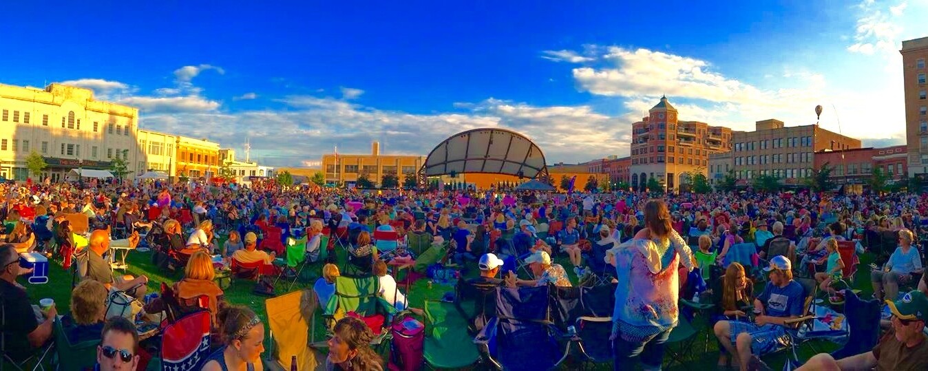 Hundreds of people gather on the grassy lawn of a central square.