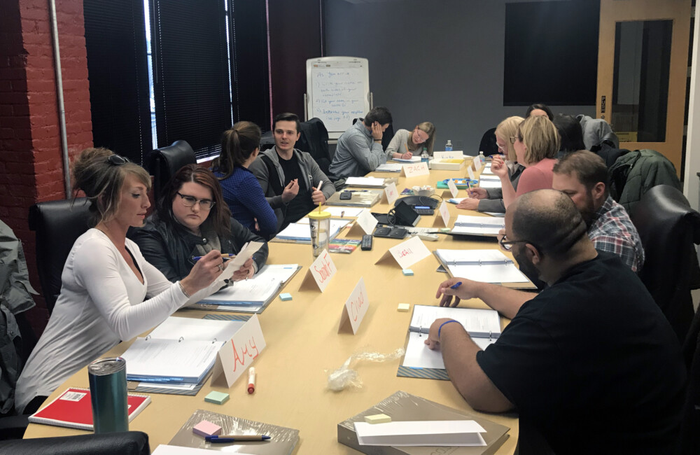 People sit around a long conference table working in pairs.