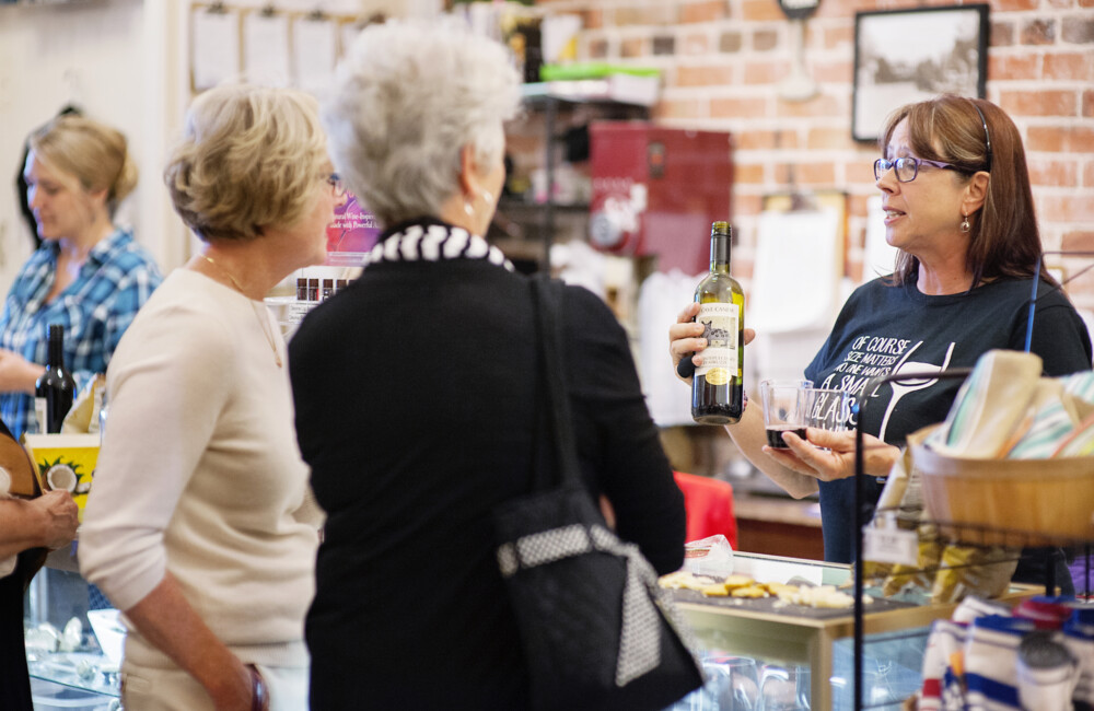 A woman serving wine to guests visiting a retail store.