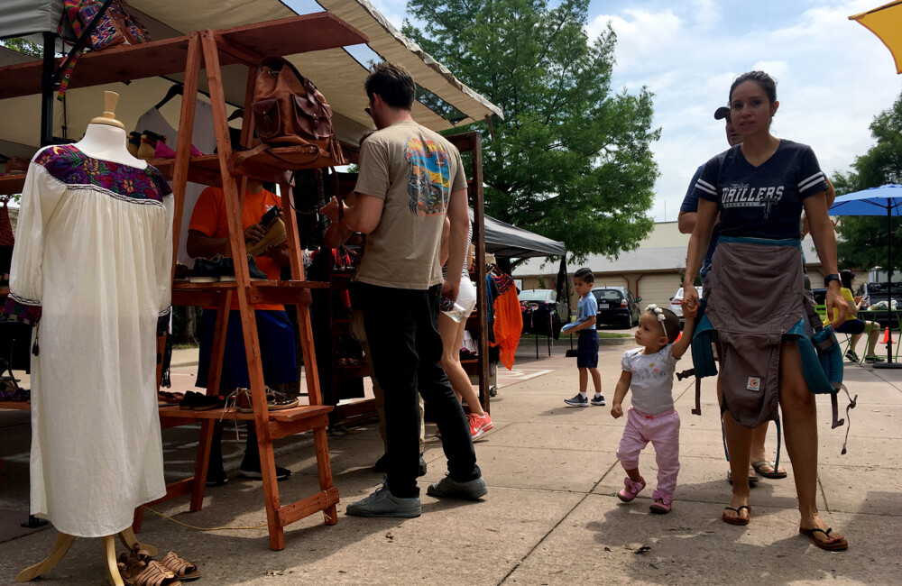 Shoppers browse vendor stalls at an outdoor marketplace.