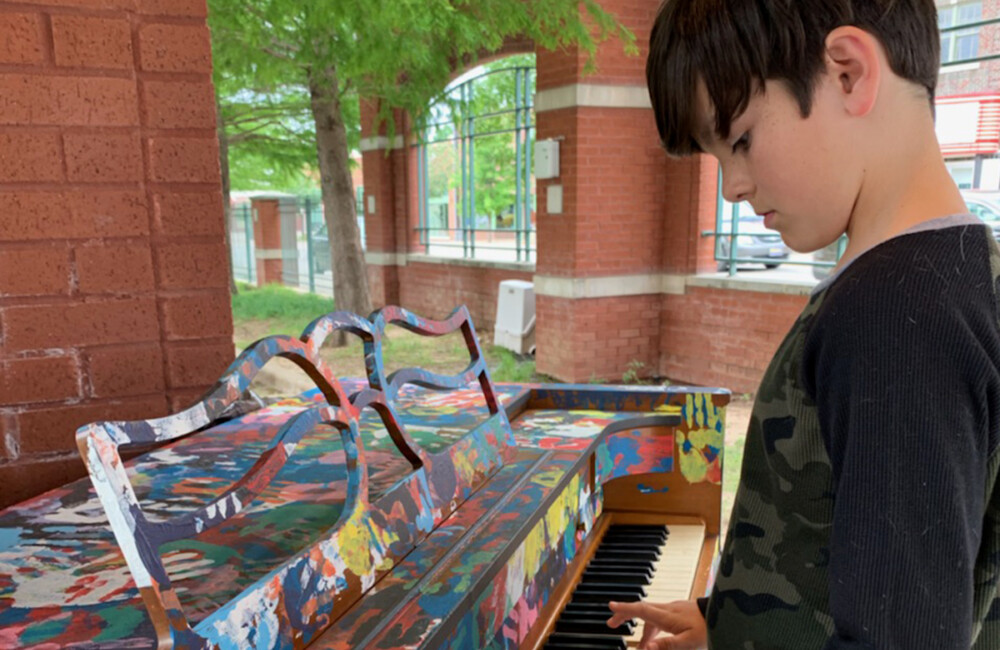 A young boy plays the public piano.