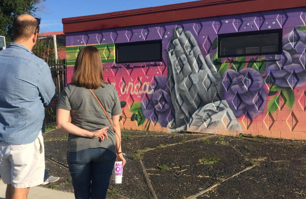 Two people look at a mural featuring flowers and a pair of hands whose palms are pressed together.