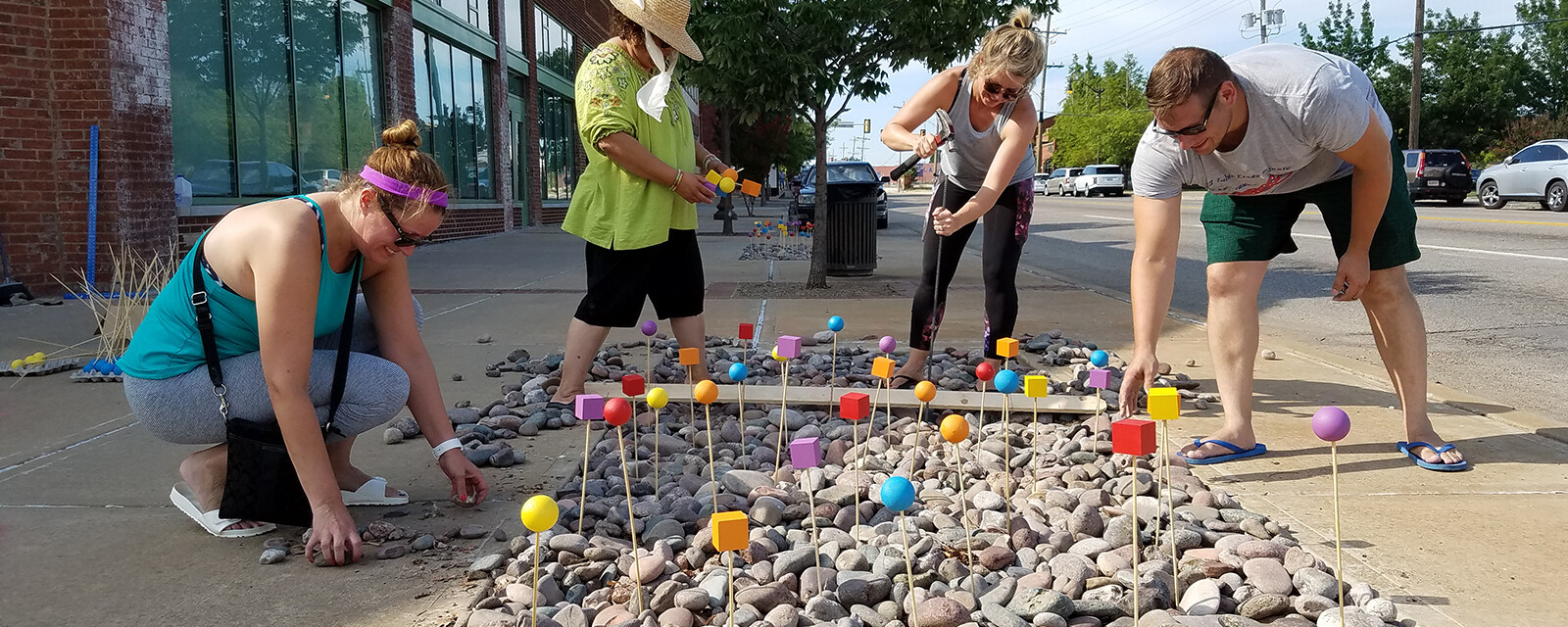 People install stakes topped with colorful toppers in a rock-filled portion of a sidewalk.