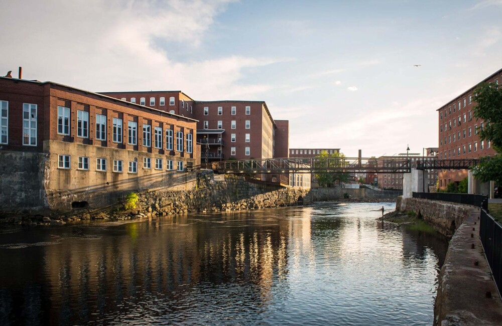 Old brick mill buildings flank both sides of a river.