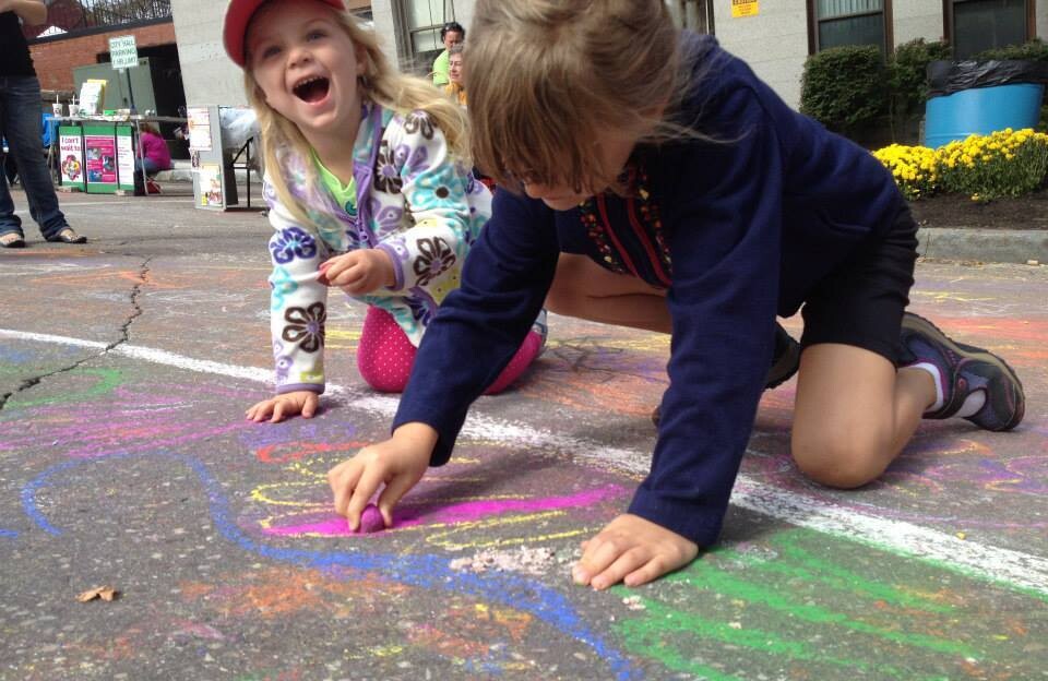 Two children gleefully use chalk to create art on a sidewalk.