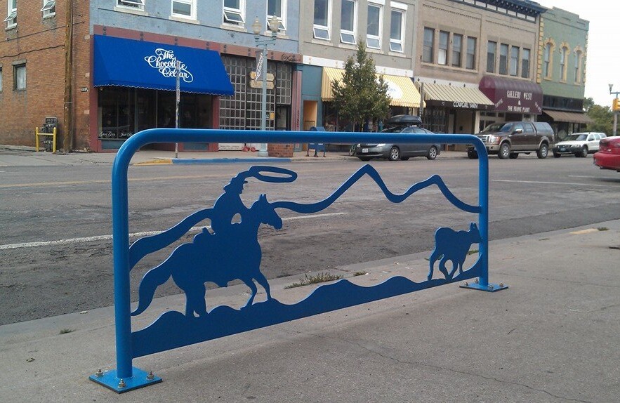 Blue metal bike rack featuring a scene depicting a cowboy on horseback chasing a calf.