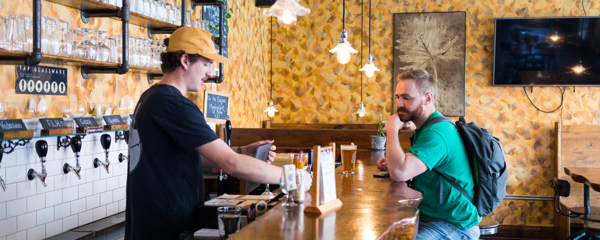 A taproom server helps a customer sitting at bar.