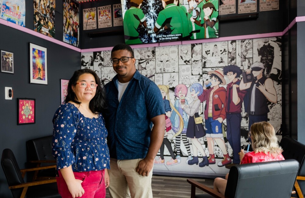 A woman and man stand side by side in the seating area of a cafe featuring anime-themed decor.