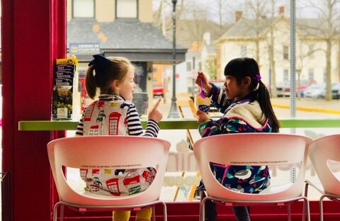 Two young girls look at each out other while gleefully eat ice cream