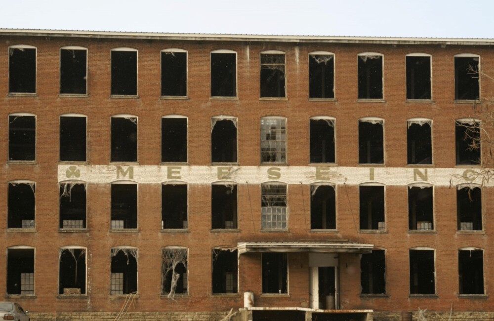 Large, historic mill building with deteriorated sign and broken windows.