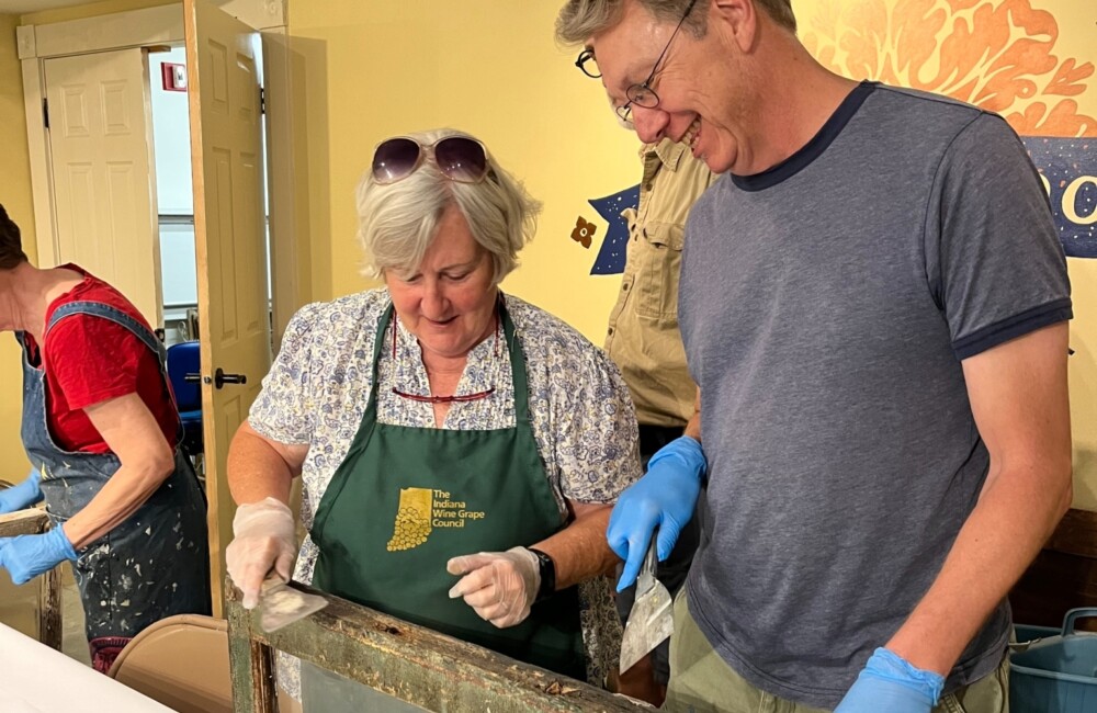 Two people perform restoration work on an old window.
