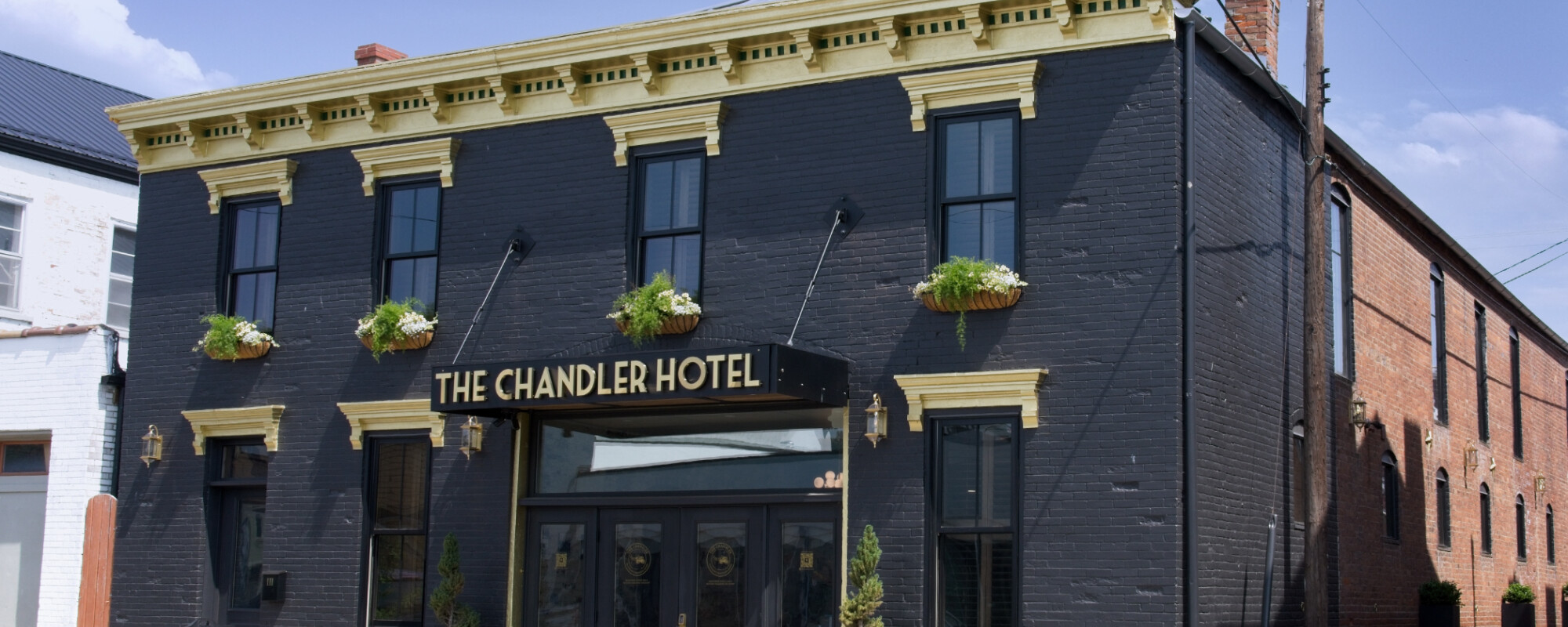 Exterior of a renovated historic building painted black with gold trim and an awning reading "The Chandler Hotel."