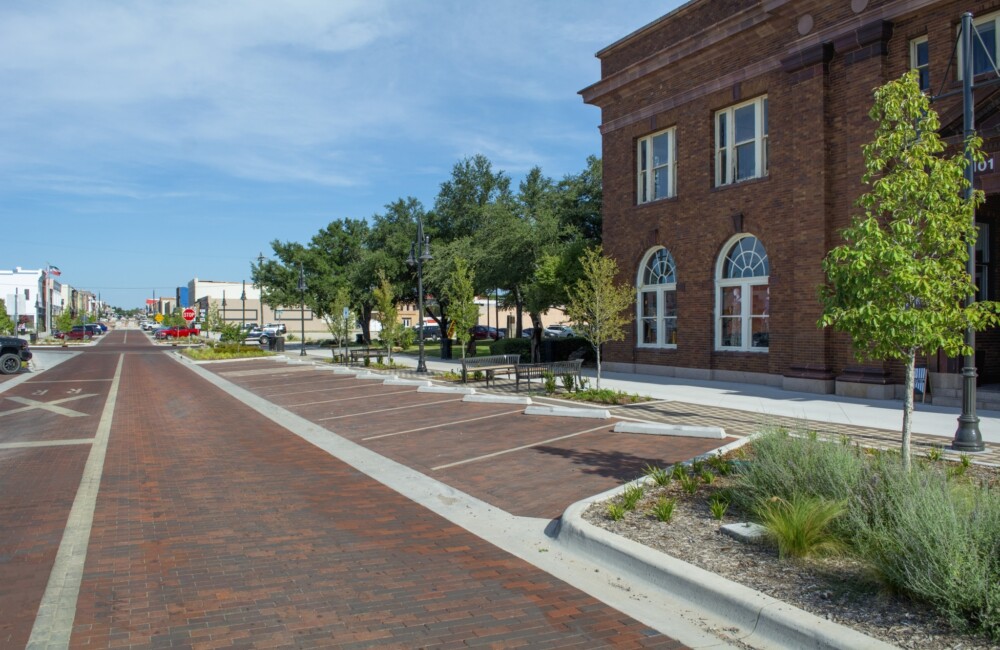 A two lane street with diagonal parking spaces, bioswales, and trees on the right.