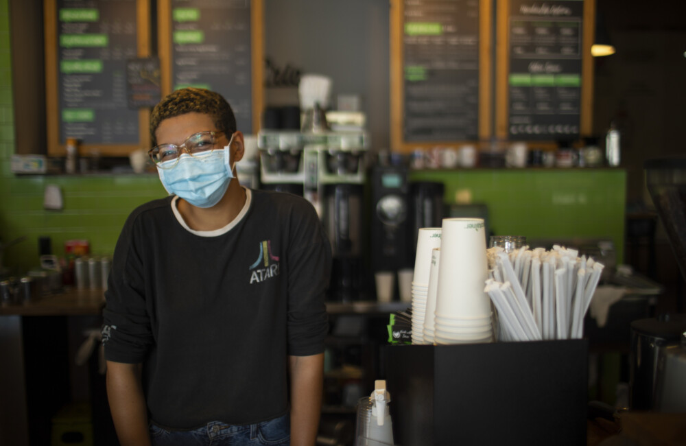 Person wearing a mask while standing behind the counter of a coffee shop.