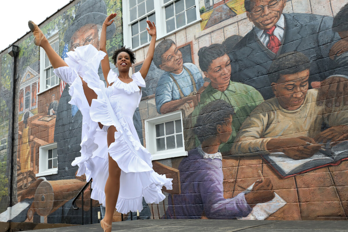 A woman dances in front of an outdoor mural featuring an educator and school children studying.