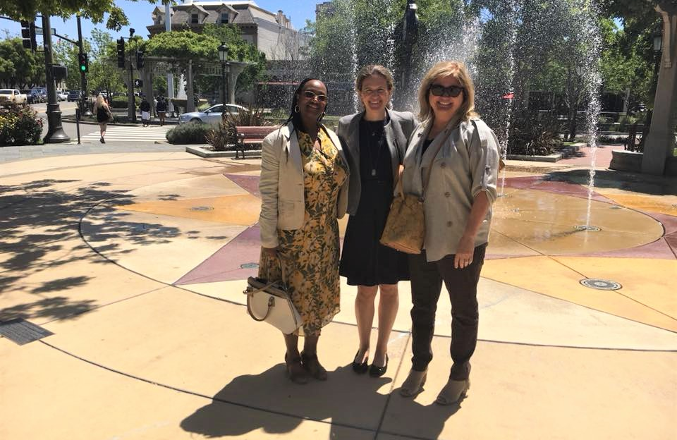 Three women posing for a group photo in front of a water fountain.