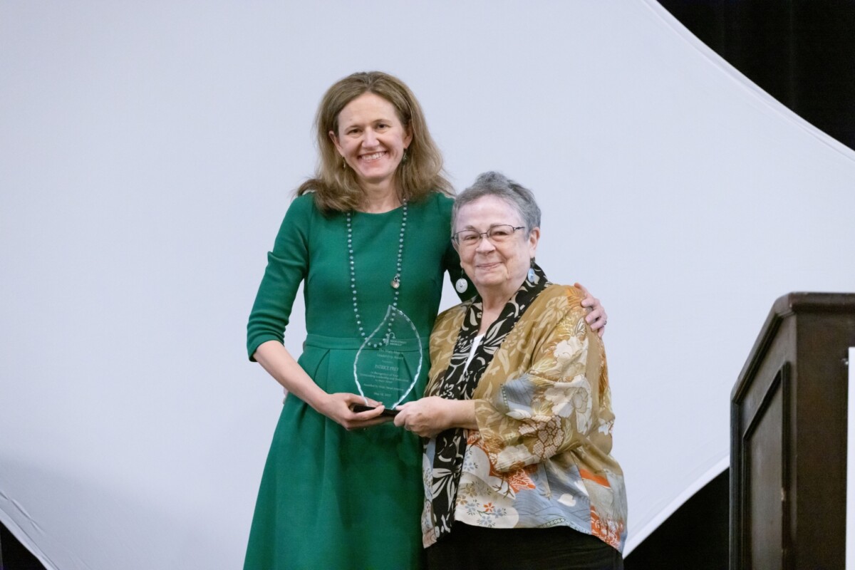 Two women stand side by side holding an award between them.