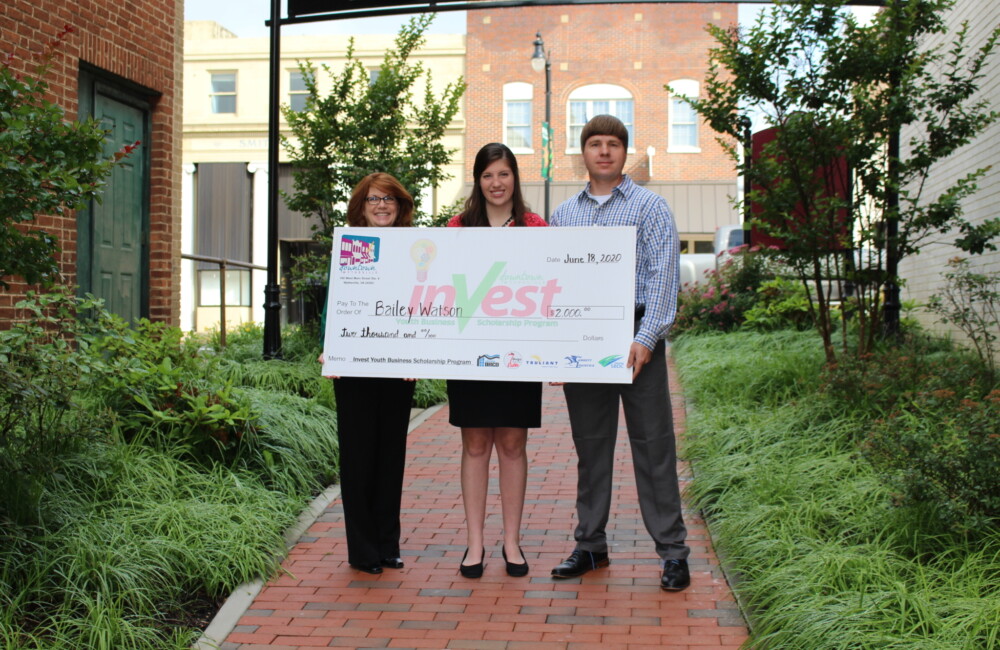 Three people standing in a courtyard while holding an oversized ceremonial check.