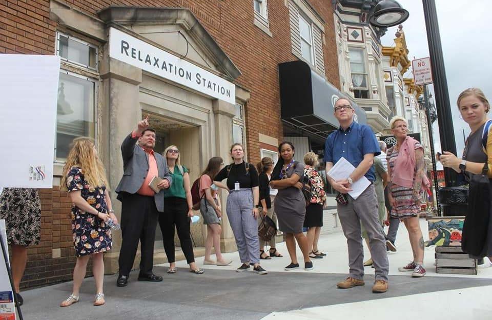 A man leads a tour group through a commercial district. The street is lined with historic buildings.
